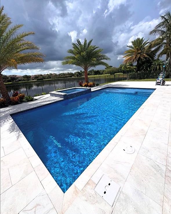 A rectangular pool and spa on a travertine deck backing onto a lake in Parkland