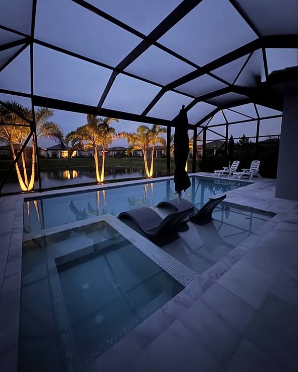 A screened pool and spa at dusk in Broward County, with uplit palms reflected in the water