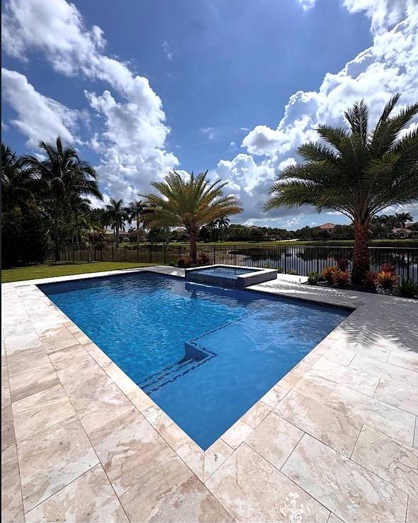 A pool and spa with palm trees and a lake behind it in Parkland, Florida